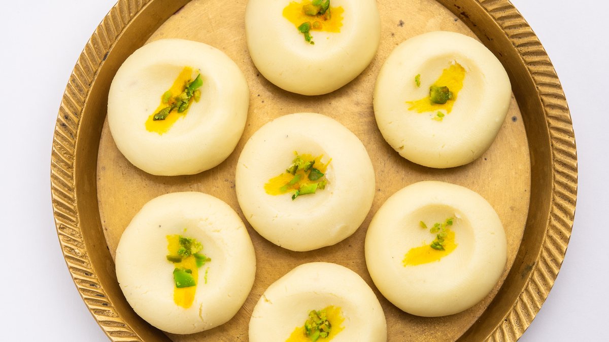 Seven round white sandesh, each with a dab of saffron and chopped pistachio, on a brass plate with a fluted rim