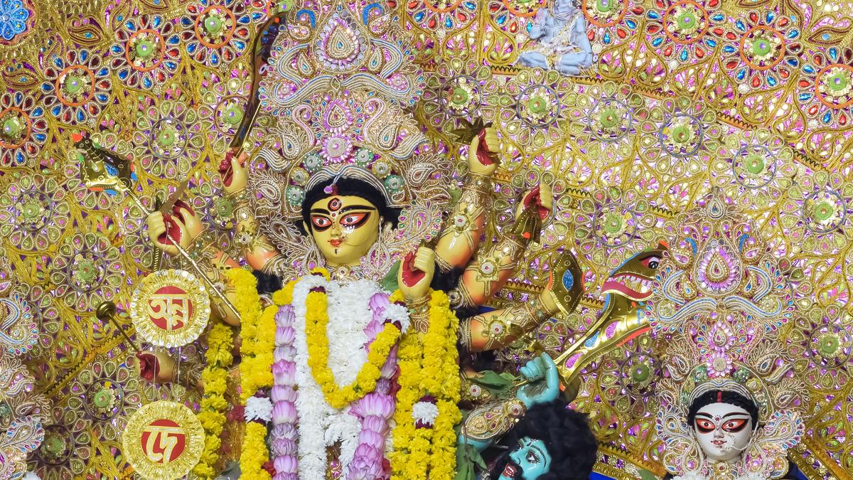 A Durga at a Delhi pandal: gold and sequinned chala behind her, lotus and marigold garlands, Mahishasura at her feet and Saraswati to the right