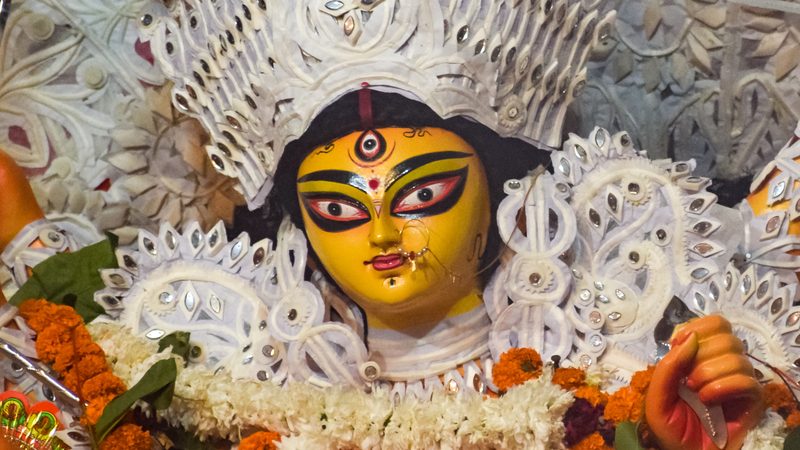 Face of a Durga idol at a South Kolkata pujo, with a white sholapith crown and marigold garlands