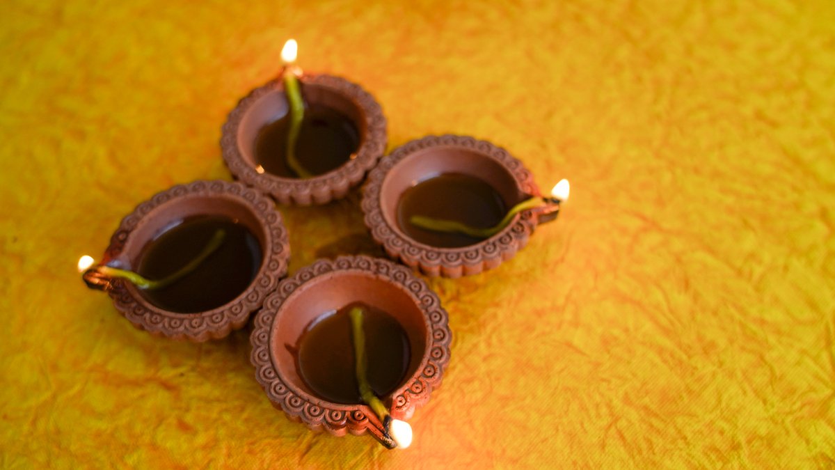 Four lit clay diyas with cotton wicks in oil, set in a small cluster on a crumpled yellow and orange cloth