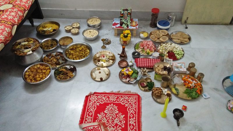 হাওড়ার এক বাড়ির মেঝেয় কোজাগরী লক্ষ্মীপুজোর আয়োজন: জলচৌকিতে ছোট্ট লক্ষ্মী, সাদা আলপনা, লাল আসন ঘিরে থালায় থালায় লুচি, নাড়ু, কাটা ফল, মিষ্টি আর রান্না করা পদ