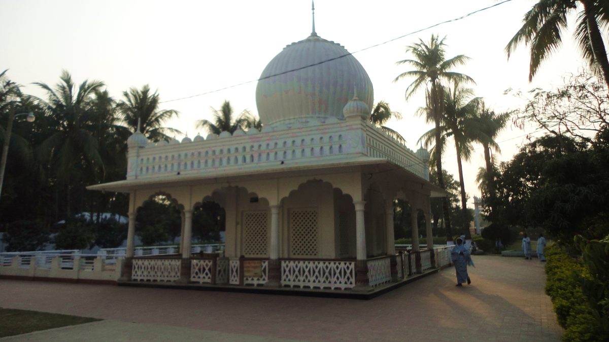 The white domed shrine of Lalon at his akhra in Cheuriya, Kushtia, with coconut palms and a visitor walking past in the evening