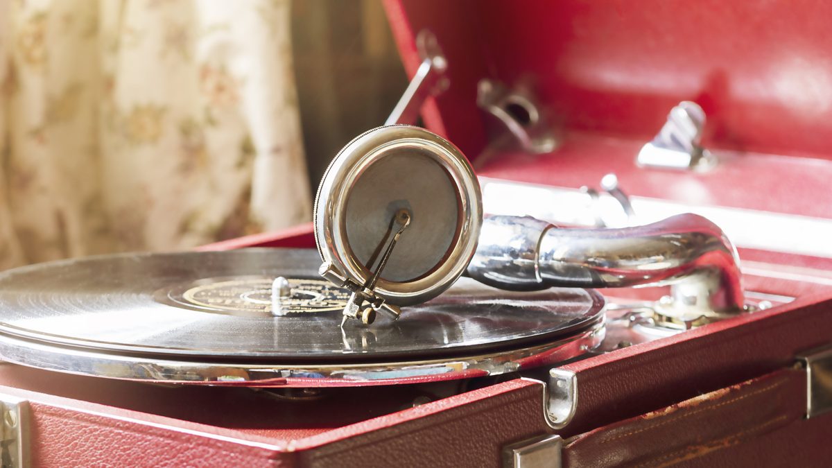 A portable wind-up gramophone in a red case, with a record on the platter and a chrome soundbox resting on it